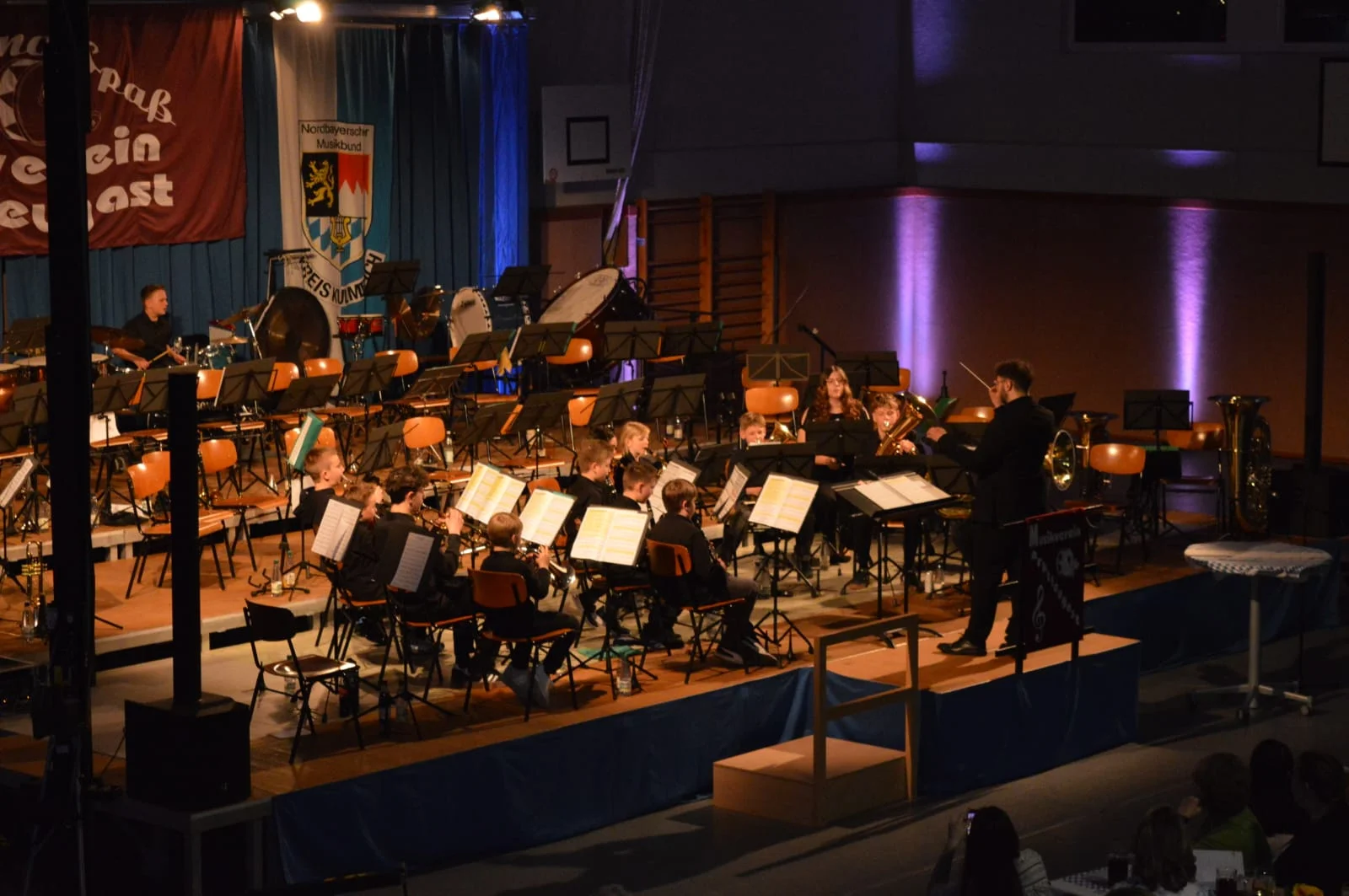Die Nachwuchskünstler sitzen auf der Bühne und spielen einfache Lieder. Davor steht der Dirigent.